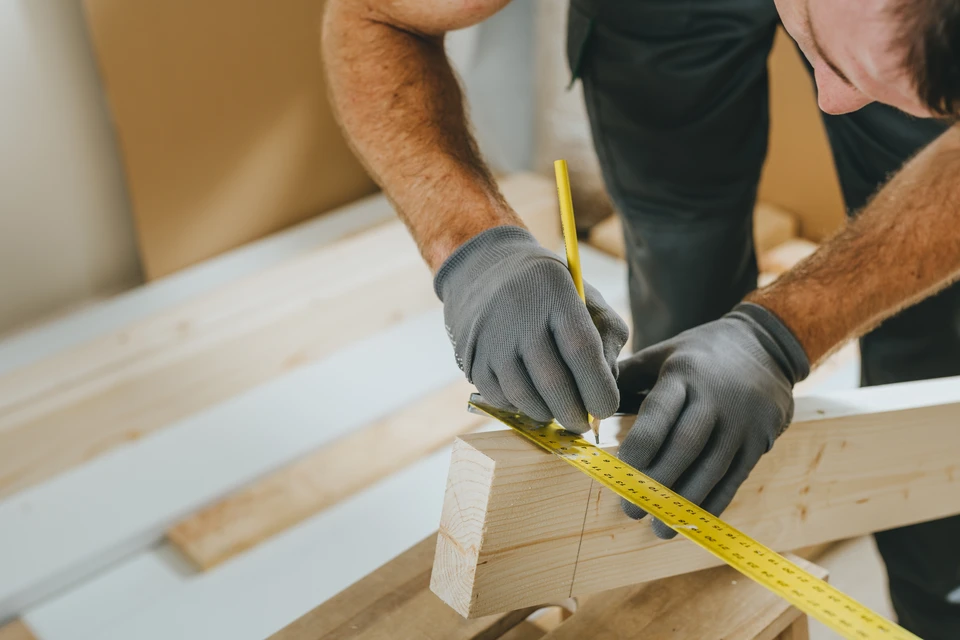 Artisan menuisier barbu en salopette examine une planche de bois dans son atelier