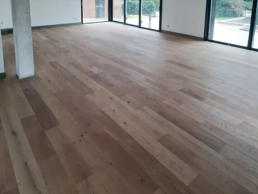 Salon moderne aux tons naturels avec fauteuil beige et coussin jaune moutarde, grande fenêtre apportant lumière naturelle, plantes vertes dépolluantes, sol parquet chêne clair, murs blancs avec lambris bois vertical