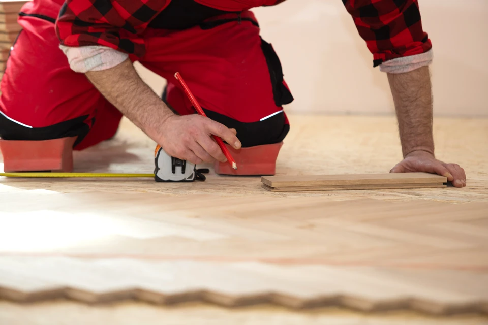 Intérieur de chantier, ouvrier en gants de protection jaunes utilisant une scie sauteuse électrique pour découper des lames de parquet stratifié